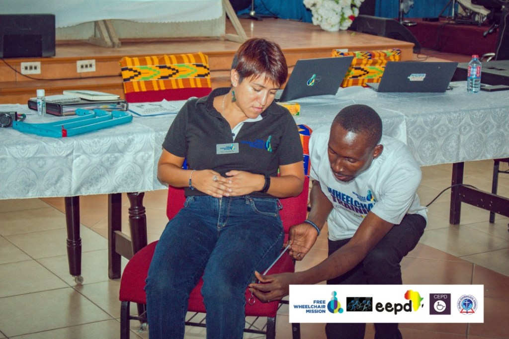 community member measuring someone's leg as they sit for a wheelchair fitting