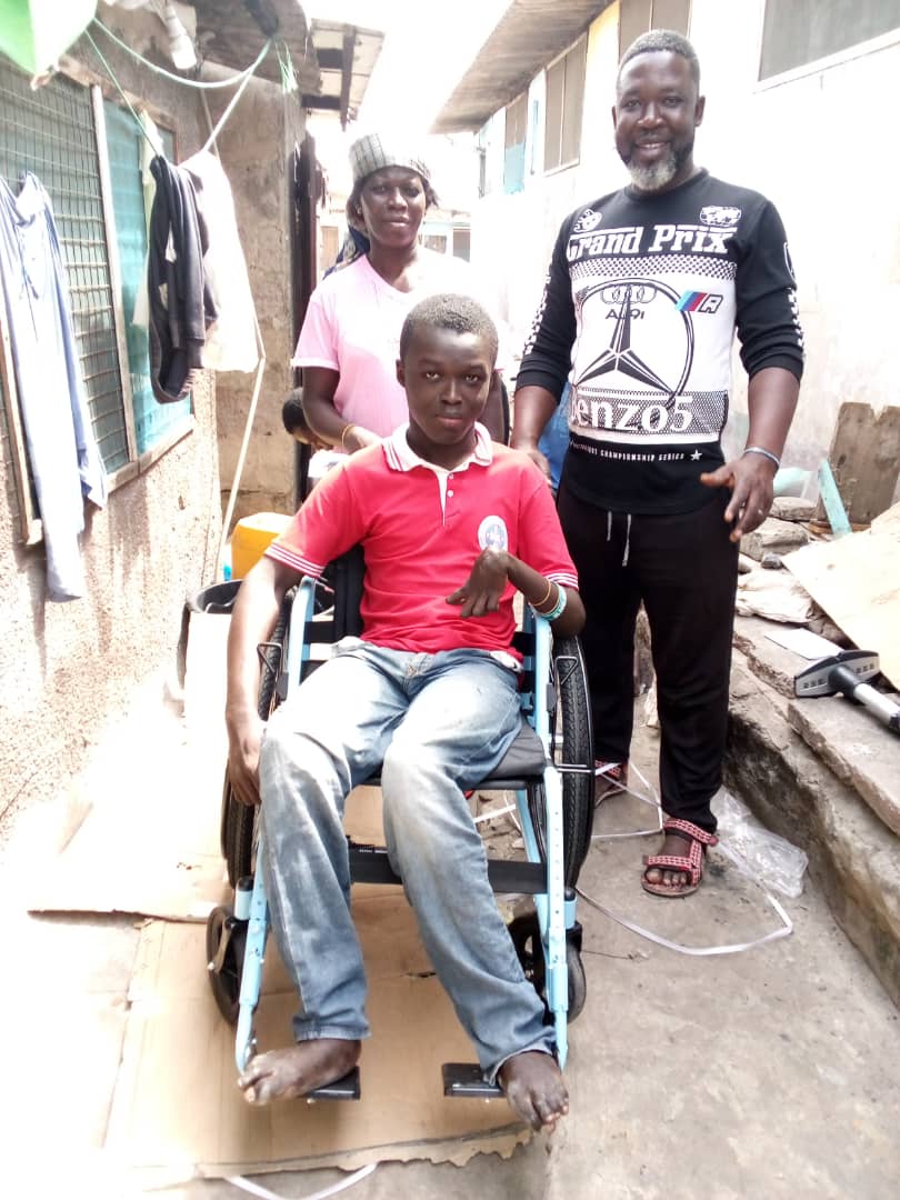 A young boy sitting in a wheelchair with two people standing behind him